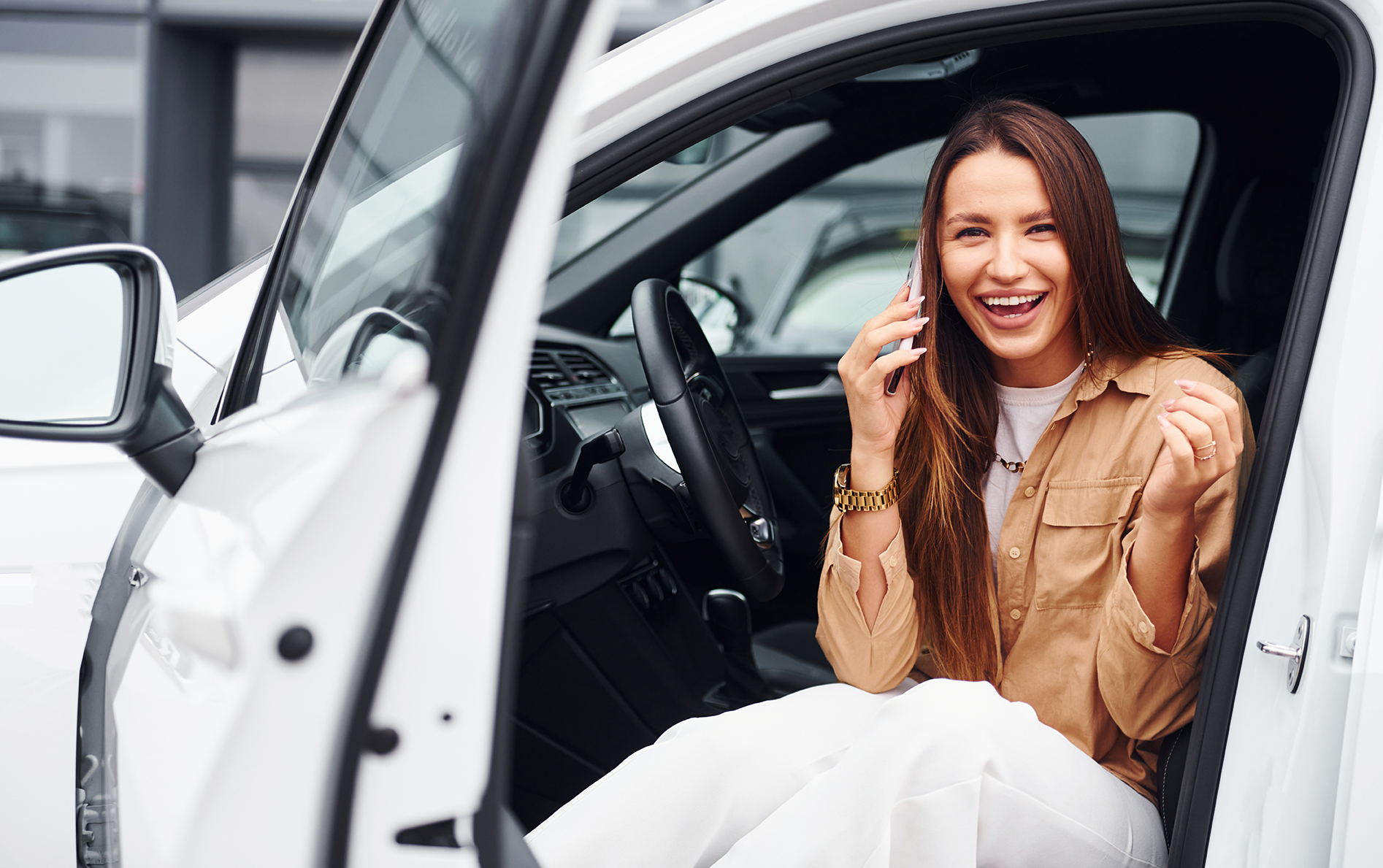 Talks by phone with door opened. Fashionable beautiful young woman and her modern automobile Person holding a clipboard inspecting a vehicle in a showroom